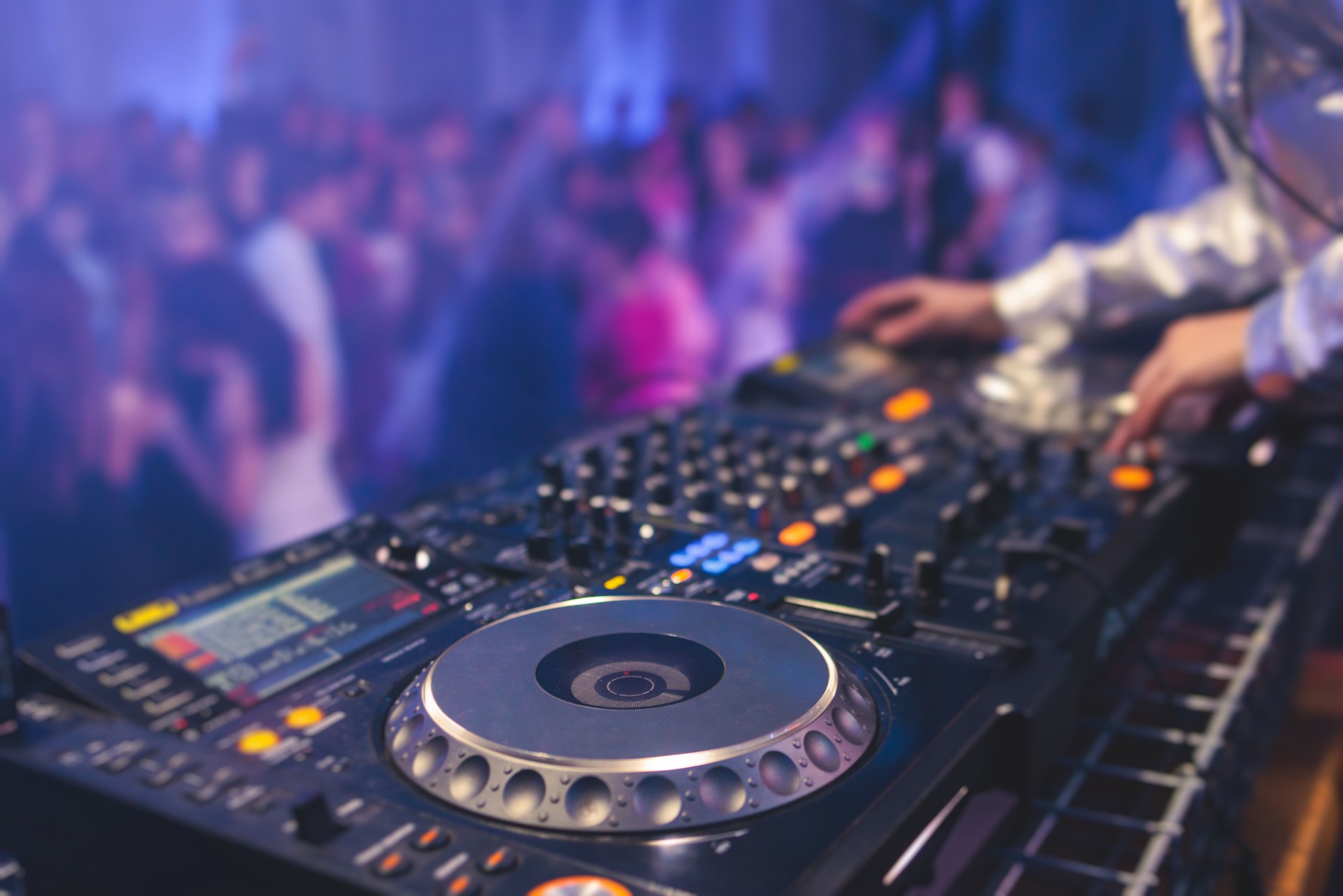View of Dj mixer and vinyl plate with headphones on a table with female girl DJ playing on stage and mixes the track in the background, during  event techno party in a night club concert hall
