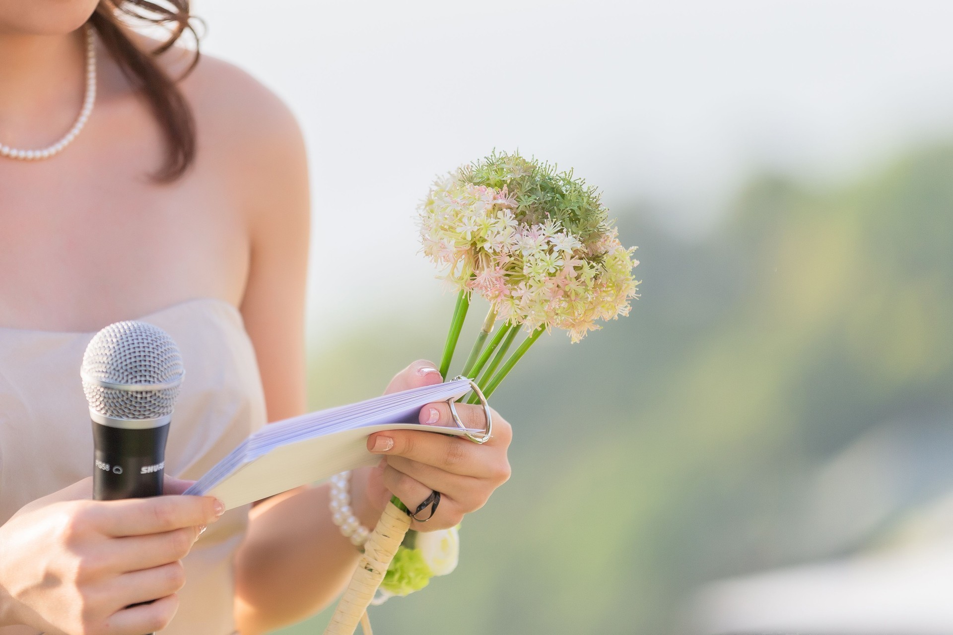 A bouquet of flowers in the hands of a female host, holding a microphone, waiting for the schedule to report the order of the event.